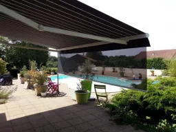 Store banne cassette aux lignes raffinées qui se distingue par son lambrequin enroulable intégré et protégé dans la barre de charge et par son éclairage à LED intégré aux bras.